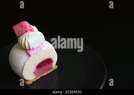 Scheibe Erdbeergelee Vanilla Mousse Kuchen auf schwarzem Teller mit Copy Space auf schwarzem Hintergrund Stockfoto