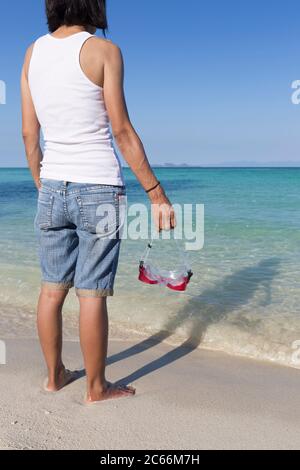 Asiatische Frau, die am Strand steht und eine Schnorchelmaske hält, Thailand Stockfoto