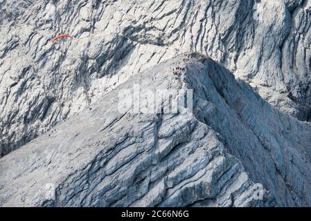 Alpspitze Peak mit Bergsteigern und Gleitschirm, Hochblassen im Hintergrund, Luftaufnahme, Garmisch-Partenkirchen, Bayern, Deutschland Stockfoto