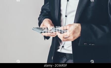 Ein Geschäftsmann in einem schwarzen Luxusanzug hält Dollar in den Händen. Der Mann zählt sein Geld. Stockfoto