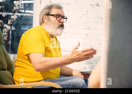 Gemütliches Sprechen. Ein paar Senioren verbringen Zeit zusammen unter Quarantäne - reifen und pensionierten Mann und Frau diskutieren, reden, trinken Tee. Augen müde von Gadgets. Gemütlicher Hausabend. Lifestyle. Stockfoto