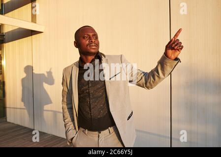 Afroamerikanischer Geschäftsmann bei Sonnenuntergang. Er zeigt mit dem Finger auf den Himmel. Stockfoto