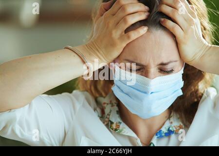 Leben während covid-19 Pandemie. Gestresste junge Frau in weißer Bluse mit medizinischer Maske. Stockfoto