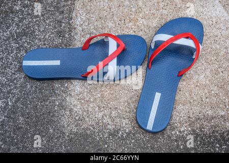 Ein Paar rot-weiße und blaue Flip-Flops, die an einem heißen Sommertag im Juli auf der Zementterrasse am Pool liegen gelassen wurden Stockfoto