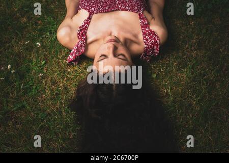Junge Frau, die auf Gras mit langen geraden Haaren liegt Stockfoto