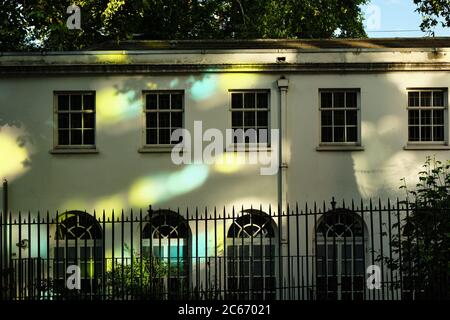 Zweistöckiges Gebäude im alten viktorianischen Stil mit Glasfenstern hinter einem schmiedeeisernen Zaun. Schöne und bunte Reflexion von Sonnenlicht auf der Fassade. Stockfoto