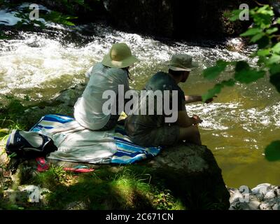 Das Paar saß auf einem Felsen am East Lyn River, Watersmeet, Devon, Großbritannien Stockfoto