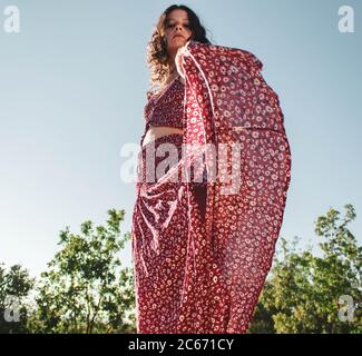 Junges Mädchen in langen roten Sommerkleid auf dem Vorbeigehen An blauem Himmel Stockfoto