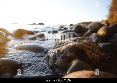 Nahaufnahme von Meereswellen, die auf einer nassen Küste brechen Steine Sommer Sonnenuntergang, Wasserspritzer, Sonnenstrahlen, Reflexionen auf Wassertropfen. Stockfoto