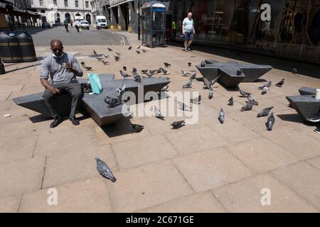 Menschen, die in einem Gebiet sitzen, in dem sich Wildtauben am 26. Juni 2020 in London, Großbritannien, in der Oxford Street versammeln. Feral Tauben, auch Stadttauben, Stadttauben oder Straßentauben genannt, sind Tauben, die von den Haustauben stammen, die in die Wildnis zurückgekehrt sind. Stockfoto
