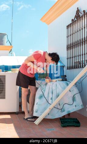 Mann, der Holz schneidet, um ein Möbelstück auf einem Dach zu bauen. Stockfoto