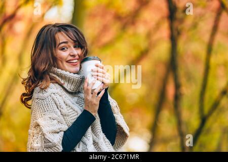 Fröhliches Mädchen hält eine Tasse heißen Kaffee im Park auf dem Spaziergang Stockfoto