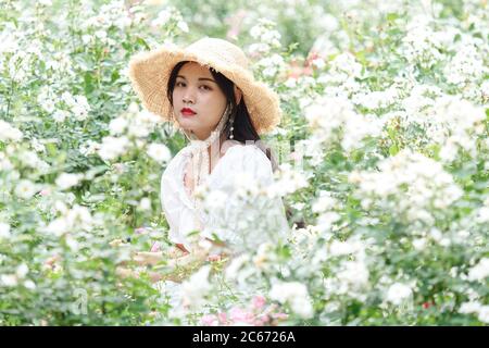 Portrait von chinesischen Mädchen in weißem Kleid sitzen zwischen weißen Blumenfeld Stockfoto