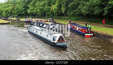 Vier schmale Boote, die zwischen den Schleusen 76 und 75 auf dem Wigan-Flug 12.6.2020 arbeiten, zwei, die den Flug hochfahren und zwei hinunter. Ein regnerischer Sommertag in Wigan Stockfoto