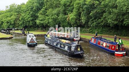 Vier schmale Boote, die zwischen den Schleusen 76 und 75 auf den Schleusen von Wigan arbeiten, zwei, die den Flug hochfahren und ein Schloss verlassen, und zwei, die in ein Schloss eintreten. Stockfoto