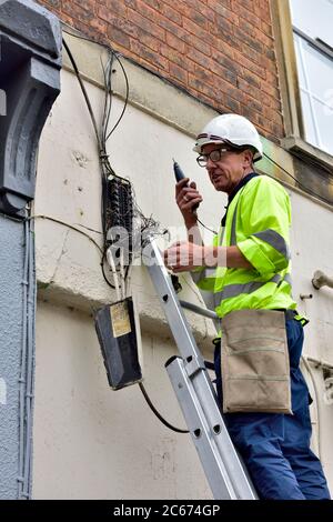 Telefoningenieur auf Leiter mit Tongenerator-Testnest von Kupferdrähten, um eine Verbindung im Hausverteiler nachzuverfolgen Stockfoto