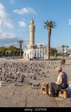 Nicht identifizierter türkischer älterer Mann, der in der Nähe des Uhrturms von Izmir auf dem Konak-Platz in der Türkei Nahrung für Tauben verkauft Stockfoto