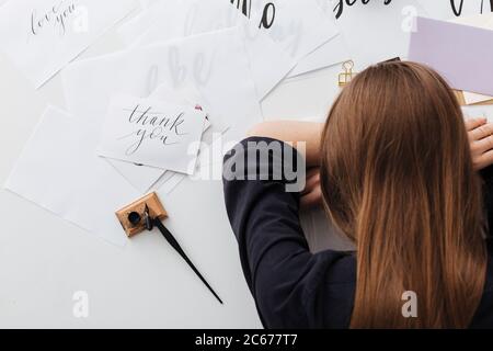 Foto einer müden Dame, die am weißen Schreibtisch sitzt und schläft, während sie den Kopf auf ihre Hände lehnt, mit klassischem Tintenstift und Notizen in der Nähe isoliert Stockfoto