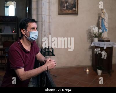 Horizontales Porträt eines Mannes mit einer chirurgischen Maske stehend und in einer Kirche zu beten Stockfoto