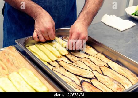 Koch macht Schichten von Gemüse zu griechischen Moussaka kochen, professionelle Küche, getönte Stockfoto