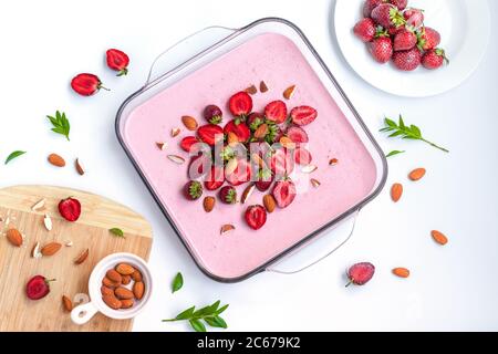 Köstliche cremige Beerensouffle Kuchen in einer Glasschale mit Erdbeeren und Mandeln auf weißem Tisch. Leckeres gesundes Frühstück, Blick von oben, flach liegend Stockfoto