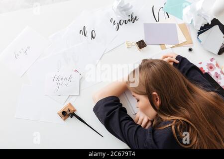 Foto einer müden Dame, die am weißen Schreibtisch sitzt und mit klassischem Tintenstift und Papieren schläft, die in der Nähe isoliert sind Stockfoto
