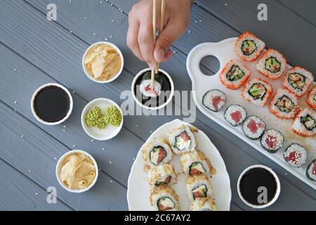 Mann, der Sushi-Brötchen isst. Sushi auf einem Holztisch im japanischen Restaurant. Nahaufnahme und Draufsicht der männlichen Hand mit Essstäbchen, die Rolle nehmen Stockfoto