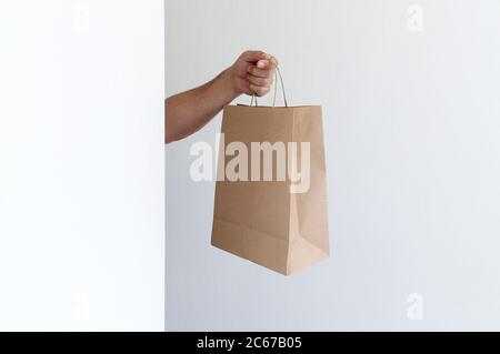 Nahaufnahme Mann hält in der Hand braun klar leer leeres Handwerk Papierbeutel zum Mitnehmen auf hellgrauem Hintergrund. Konzept der Verpackungs- und Lieferservices Stockfoto