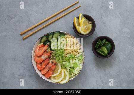 Asiatischer Salat mit Essstäbchen Draufsicht. Garnelen Poke Schüssel auf grauen Stein Hintergrund. Gesundes und ausgewogenes Lebensmittelkonzept Stockfoto