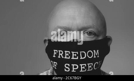 Kahlköpfiger Mann mittleren Alters trägt eine Gesichtsmaske, auf der die Worte Redefreiheit ironisch gedruckt sind Stockfoto