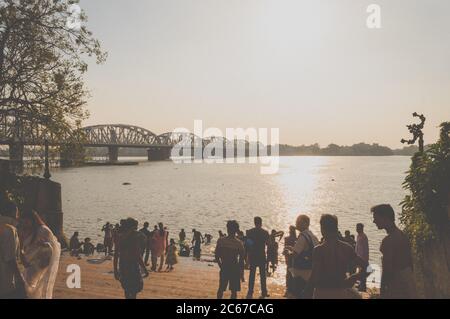 Dakshineswar Kali Mandir Temple Ghat auf dem Ufer des Holi Ganges. Zeit bei Sonnenuntergang. Überfüllte Menschen, die Abendrituale machen. Sonnenuntergang Blick mit Silhouette Railw Stockfoto