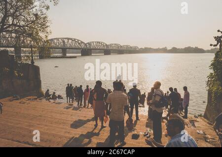 Dakshineswar Kali Mandir Temple Ghat auf dem Ufer des Holi Ganges. Zeit bei Sonnenuntergang. Überfüllte Menschen, die Abendrituale machen. Sonnenuntergang Blick mit Silhouette Railw Stockfoto