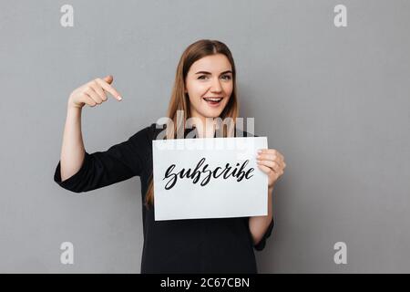 Portrait von schönen lächelnden Mädchen stehen und halten Postkarte auf grauem Hintergrund Stockfoto