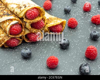 Crepes gefüllt mit Marmelade und frischen Himbeeren und Heidelbeeren auf schwarzem Schiefer Stockfoto