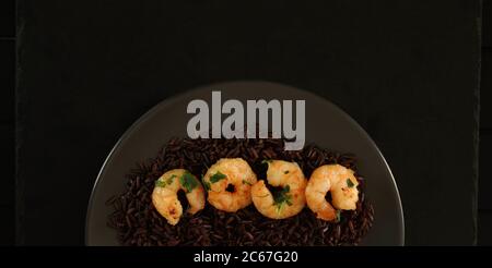 Gesundes Lebensmittelkonzept. Ein Gericht mit schwarzem Reis mit Garnelen auf dunklem Hintergrund. Draufsicht. Stockfoto