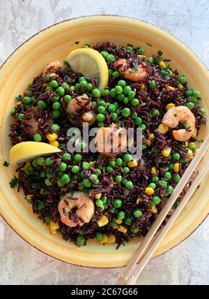 Sommerliches Speisekonzept. Kalter schwarzer Reissalat mit Mais, Erbsen, Garnelen und Zitrone auf gelbem Teller. Gesunde Ernährung. Draufsicht. Stockfoto