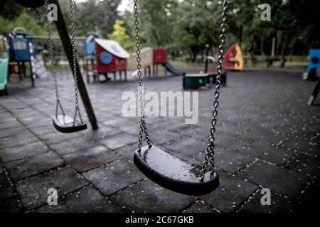 Plastik und nasse Schaukeln auf einem leeren Spielplatz während eines regnerischen Sommertages. Stockfoto