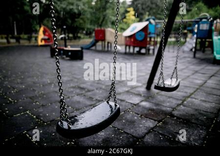 Plastik und nasse Schaukeln auf einem leeren Spielplatz während eines regnerischen Sommertages. Stockfoto