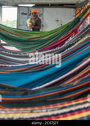 Amazonas-Fluss, Peru - 12. Dez 2017: Der Mann in der Spitzenkappe steht hinter schönen, bunten Hängematten auf dem Frachtschiff. Amazonien, Weg vom Weihnachtsmann Stockfoto