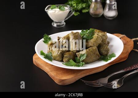 Dolma - gefüllte Traubenblätter mit Reis und Fleisch auf einem weißen Teller auf Holzbrett. Traditionelle kaukasische, griechische, osmanische und türkische Küche, Closeup Stockfoto