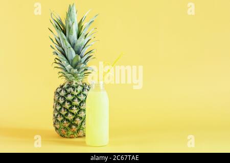 Ananassaft in Glasflasche mit Stroh und Ananasfrucht auf gelbem Hintergrund. Erfrischungscocktail im Sommer. Speicherplatz kopieren. Stockfoto