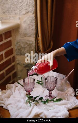 Eine Frauenhand gießt ein rotes Getränk aus einer Flasche in ein Glas. Stockfoto