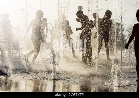 Silhouetten von fröhlichen Kindern spielen in Wasserbrunnen an heißen Sommertagen. Happy Kindheitskonzept. Rücklicht Stockfoto