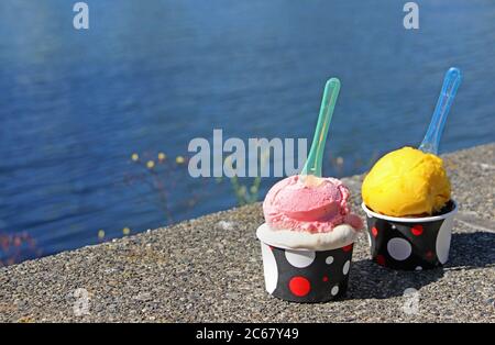 Sommer-Snacks: Zwei Tassen Eis. Ozean im Hintergrund. Der Blick auf zwei Kugeln in den Tassen mit Löffel - ein erdbeer und ein Mango Geschmack. Stockfoto