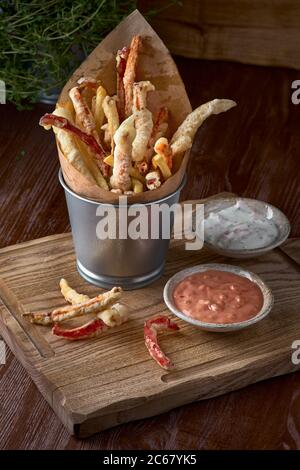 Essen zum Mitnehmen. pommes Frites und Gemüse in Teig, Karotten, Paprika, geräuchert und Saucen auf einem Holzbrett Stockfoto