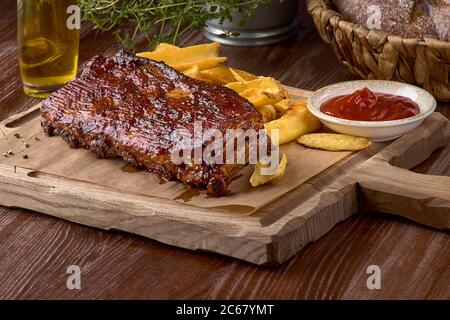 Würzige gegrillte Schweineribs mit pommes auf dem Schneidebrett. Leckere Vorspeise für Bier auf dunklem Hintergrund Stockfoto
