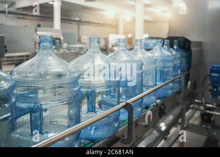 PET-Flaschen oder Gallonen aus Kunststoff auf Produktionslinie oder Förderband in der Wasserfabrik zum Abfüllen von reinem Trinkwasser. Stockfoto