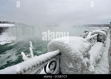 Kunstvolle Geländer entlang der Kante der Niagara-Fälle, die durch den Nebel der Wasserfälle mit dickem, weißem Eis bedeckt sind. Hufeisenfälle und der Nebel sind zu sehen. Stockfoto
