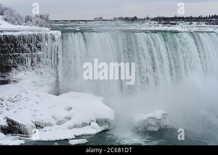 Ein Teil des Horseshoe fällt im Winter. Eiszapfen hängen von der Felswand nahe dem Wasserfall. Bäume und Felsbrocken mit Schnee bedeckt. Niagara Falls. Stockfoto