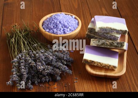 Meersalz mit Lavendel in einer Bambusschale befinden sich Seife aus Lavendel, Olivenöl und Kakaobutter auf einem Bambusteller und getrocknete Lavendelblüten Stockfoto